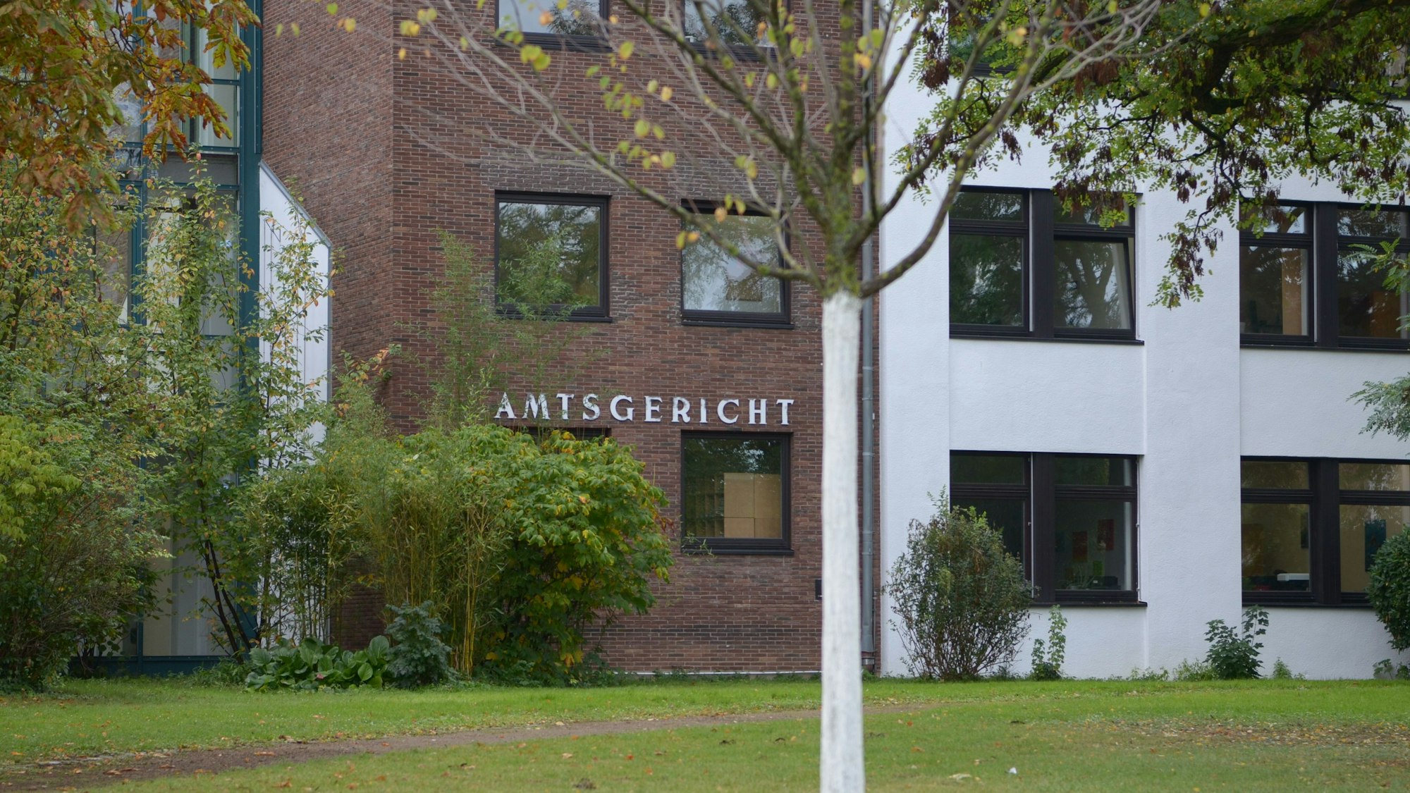 Das Bild zeigt das Gerichtsgebäude hinter Bäumen und Sträuchern.