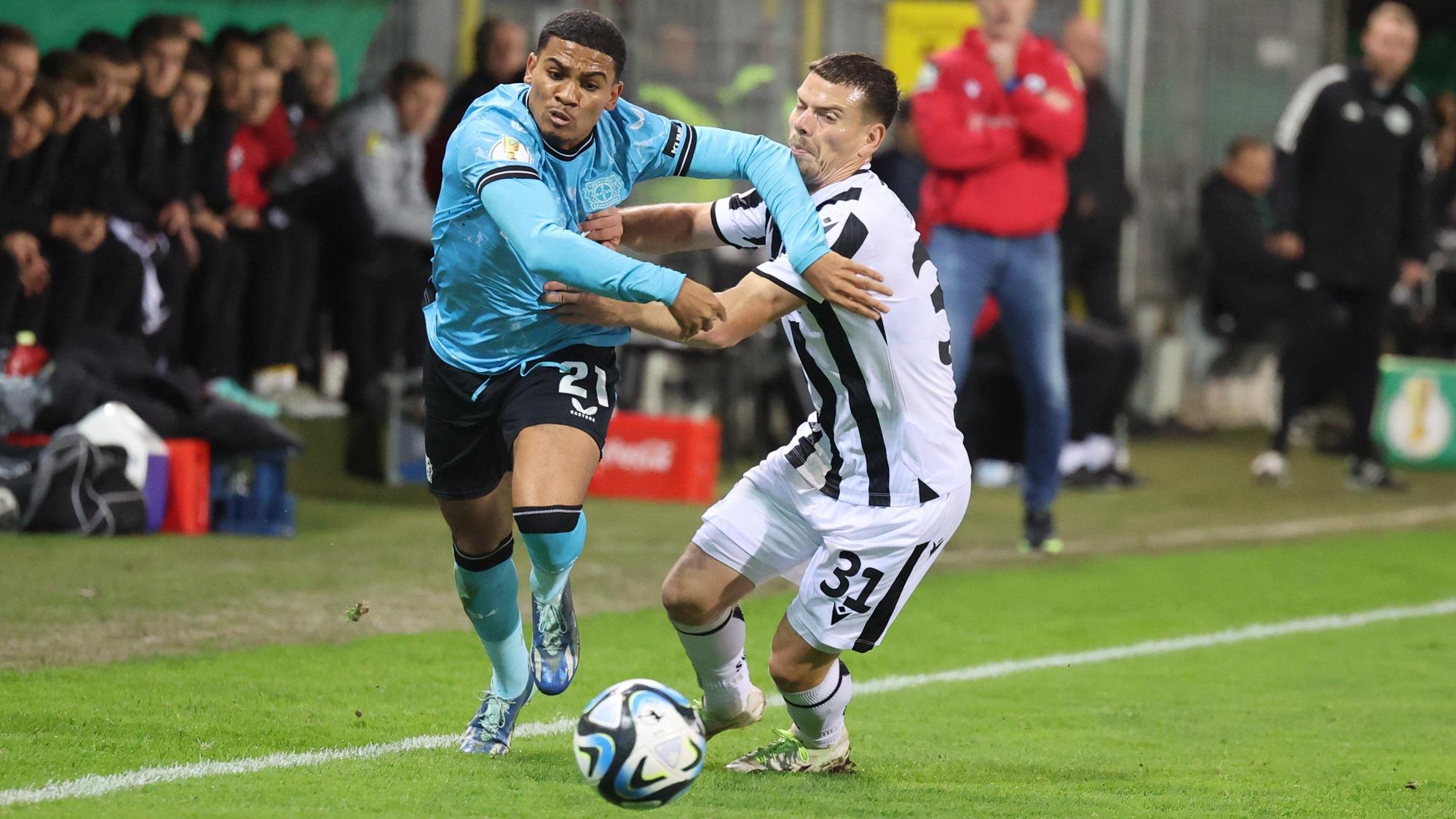 01.11.2023, Baden-Württemberg, Sandhausen: Fußball, DFB-Pokal, SV Sandhausen - Bayer Leverkusen, 2. Runde, BWT-Stadion am Hardtwald: Leverkusens Amine Adli (l) und Sandhausens Jonas Weik in Aktion. Foto: Jörg Halisch/dpa - WICHTIGER HINWEIS: Gemäß den Vorgaben der DFL Deutsche Fußball Liga bzw. des DFB Deutscher Fußball-Bund ist es untersagt, in dem Stadion und/oder vom Spiel angefertigte Fotoaufnahmen in Form von Sequenzbildern und/oder videoähnlichen Fotostrecken zu verwerten bzw. verwerten zu lassen. +++ dpa-Bildfunk +++