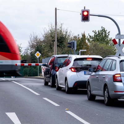 Das Bild zeigt einen Zug, der einen Bahnübergang passiert. Autos stehen vor der geschlossenen Schranke.