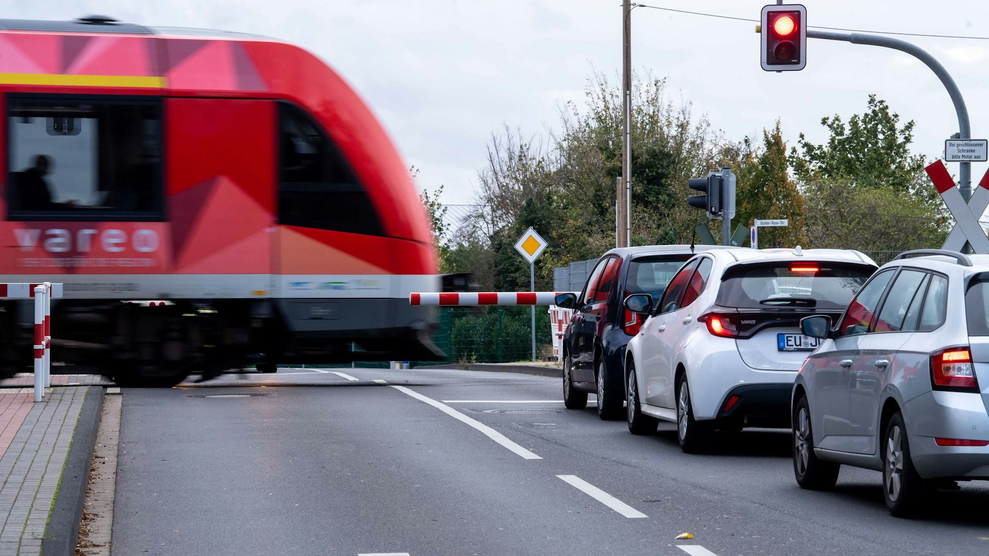 Das Bild zeigt einen Zug, der einen Bahnübergang passiert. Autos stehen vor der geschlossenen Schranke.