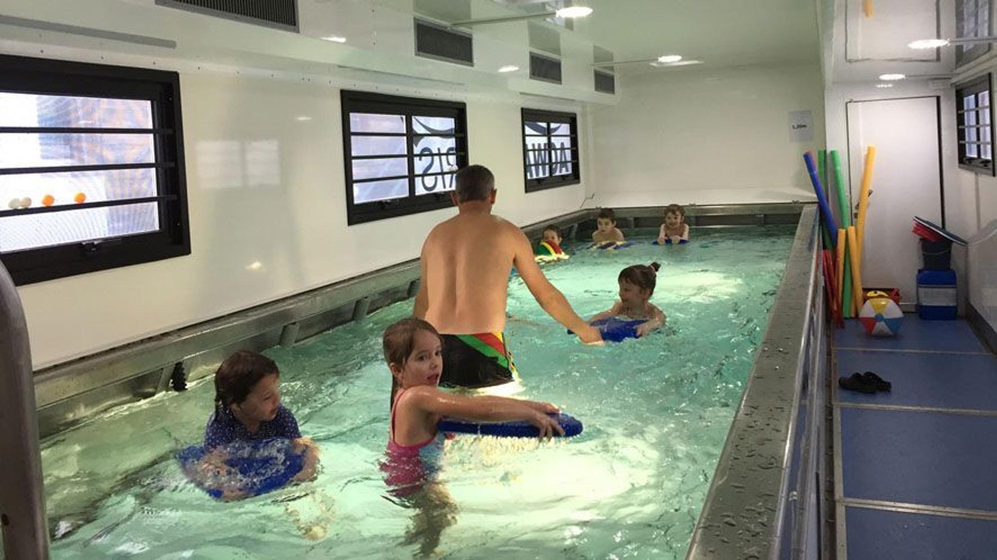 Kinder schwimmen in einem kleinen Becken in einem umgebauten Übersee-Container.