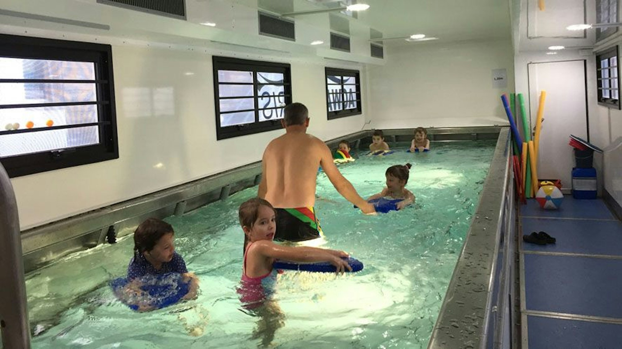 Kinder schwimmen in einem kleinen Becken in einem umgebauten Übersee-Container.