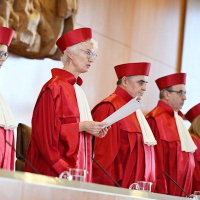 Fünf Richterinnen und Richter des Bundesverfassungsgerichts in roter Robe stehen bei der Verkündung des Urteils zur Verfassungsmäßigkeit der Reform zur Wiederaufnahme von Strafverfahren durch die Vorsitzende Doris König.