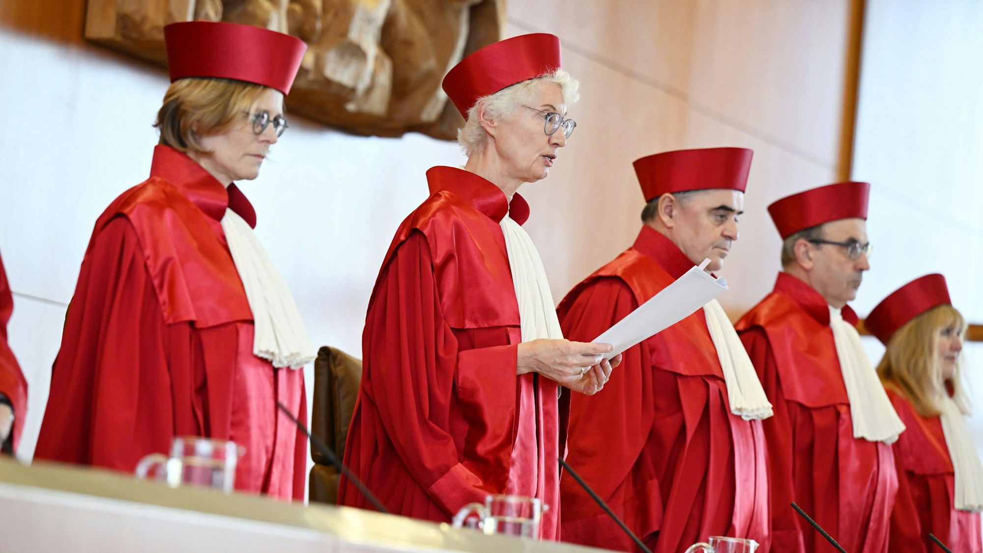 Fünf Richterinnen und Richter des Bundesverfassungsgerichts in roter Robe stehen bei der Verkündung des Urteils zur Verfassungsmäßigkeit der Reform zur Wiederaufnahme von Strafverfahren durch die Vorsitzende Doris König.
