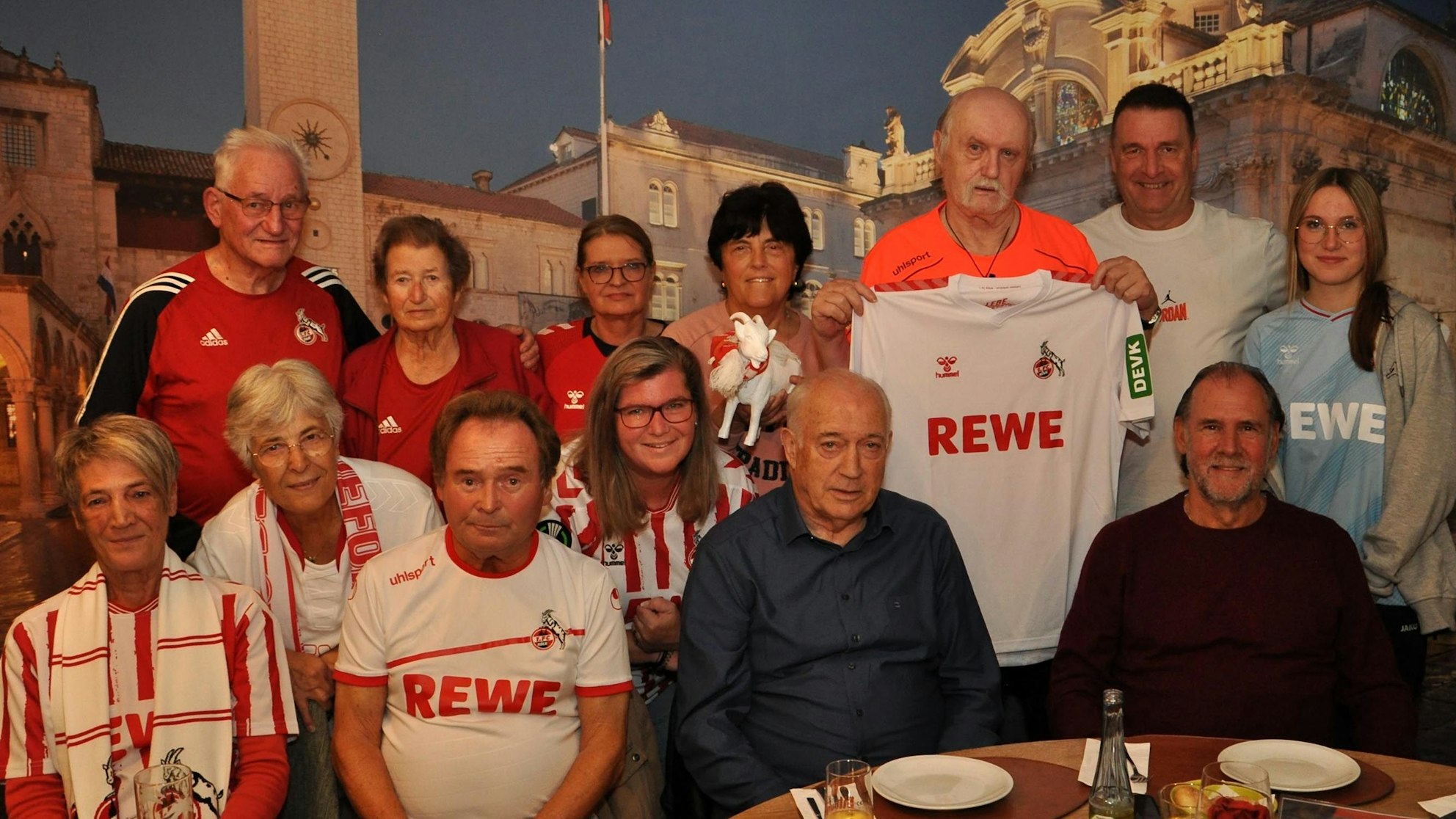 Mitglieder des 1. FC Köln Fanclubs Geißböcke Nordeifel posieren mit Bernd Cullmann und Herbert „Zimbo“ Zimmermann für ein Foto. Viele tragen FC-Trikots.