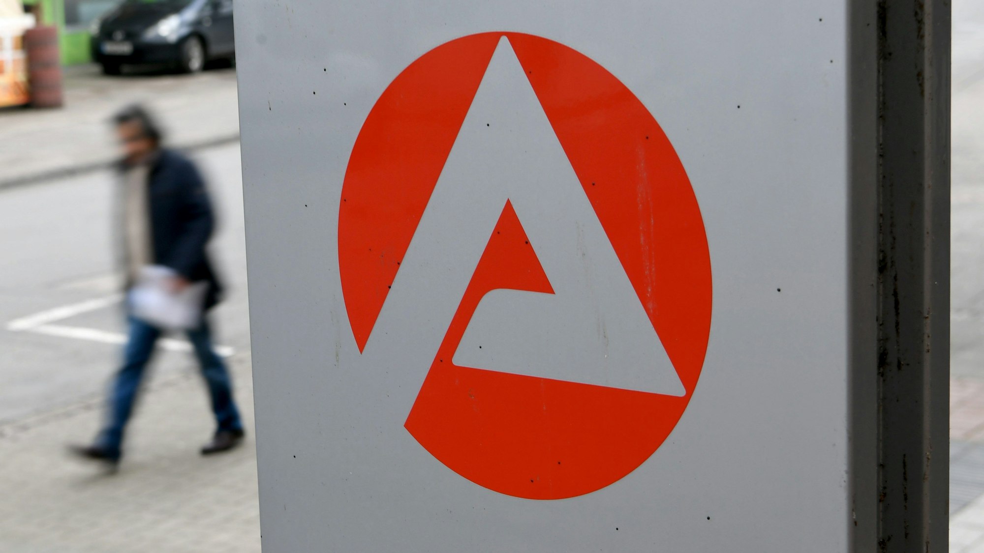 Ein Mann geht an einem Schild der Agentur für Arbeit vorbei.