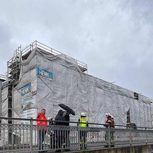 Mehrere Menschen stehen auf einer Brücke vor dem mit einem Gerüst umbauten Johannes-Sturmius-Gymnasium in Schleiden.