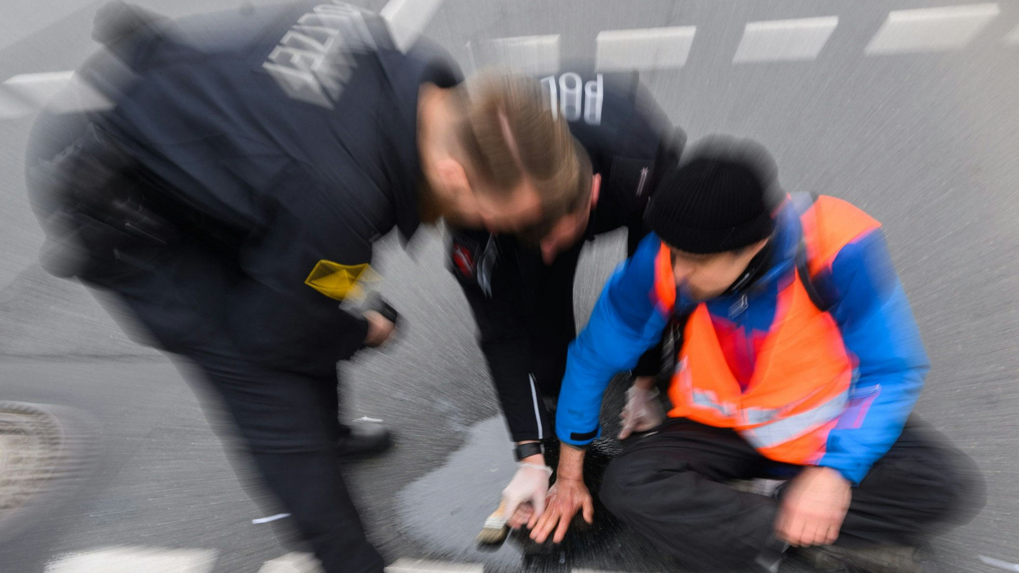 Polizisten versuchen festgeklebte Hände von Aktivisten der Gruppierung „Letzte Generation“ in Hannover mit Speiseöl von der Straße abzulösen.