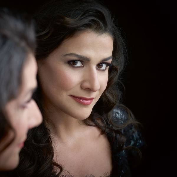 Eine Nahaufnahme von Cecilia Bartoli. Sie hat dunkle, gewellte Haare und braune Augen. Sie trägt Lippenstift und ein schwarzes Kleid.