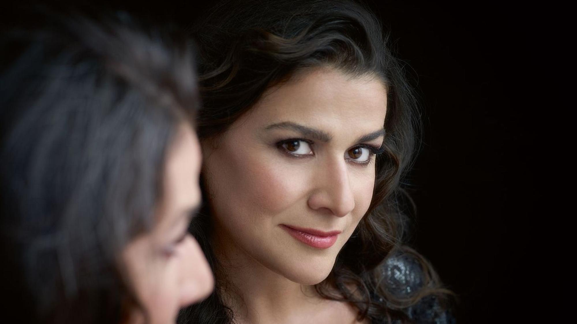 Eine Nahaufnahme von Cecilia Bartoli. Sie hat dunkle, gewellte Haare und braune Augen. Sie trägt Lippenstift und ein schwarzes Kleid.