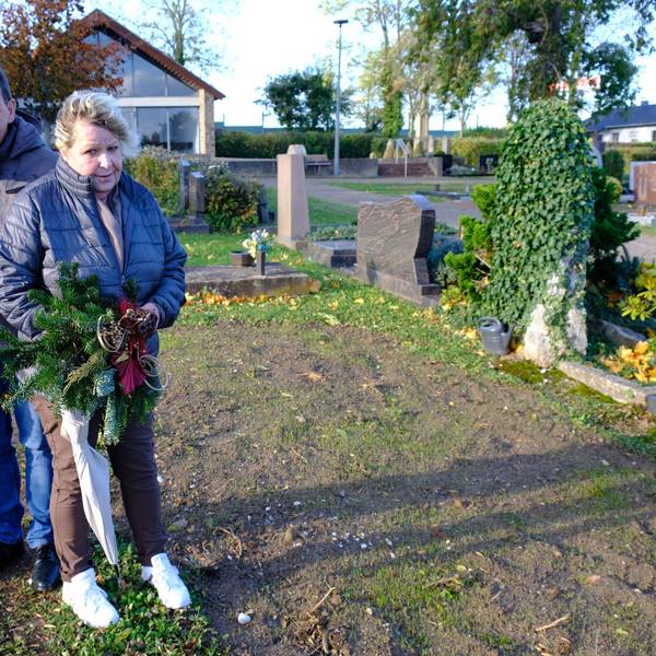 Gabi Große, Bernhard Hoffmann und Anja Hoffmann stehen auf dem Friedhof in Kommern an der Stelle, wo sich bis vor Kurzem noch das Grab ihrer Schwester Sabine befand. Gabi Große hält ein Grabgesteck in der Hand.