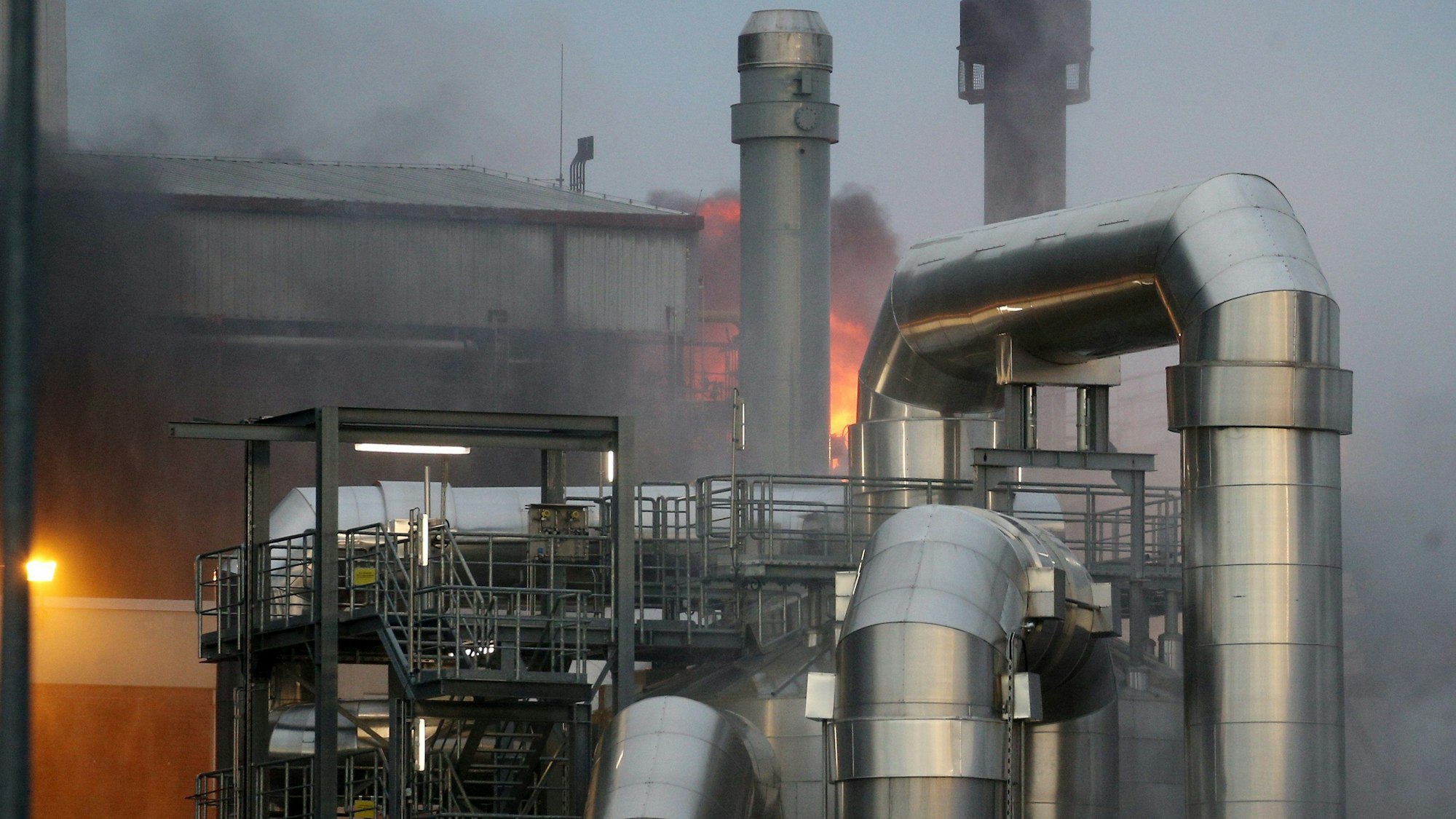 Auf einem Industriegelände ist dichter, dunkler Rauch zu sehen - im Hintergrund ist eine große Flamme erkennbar.
