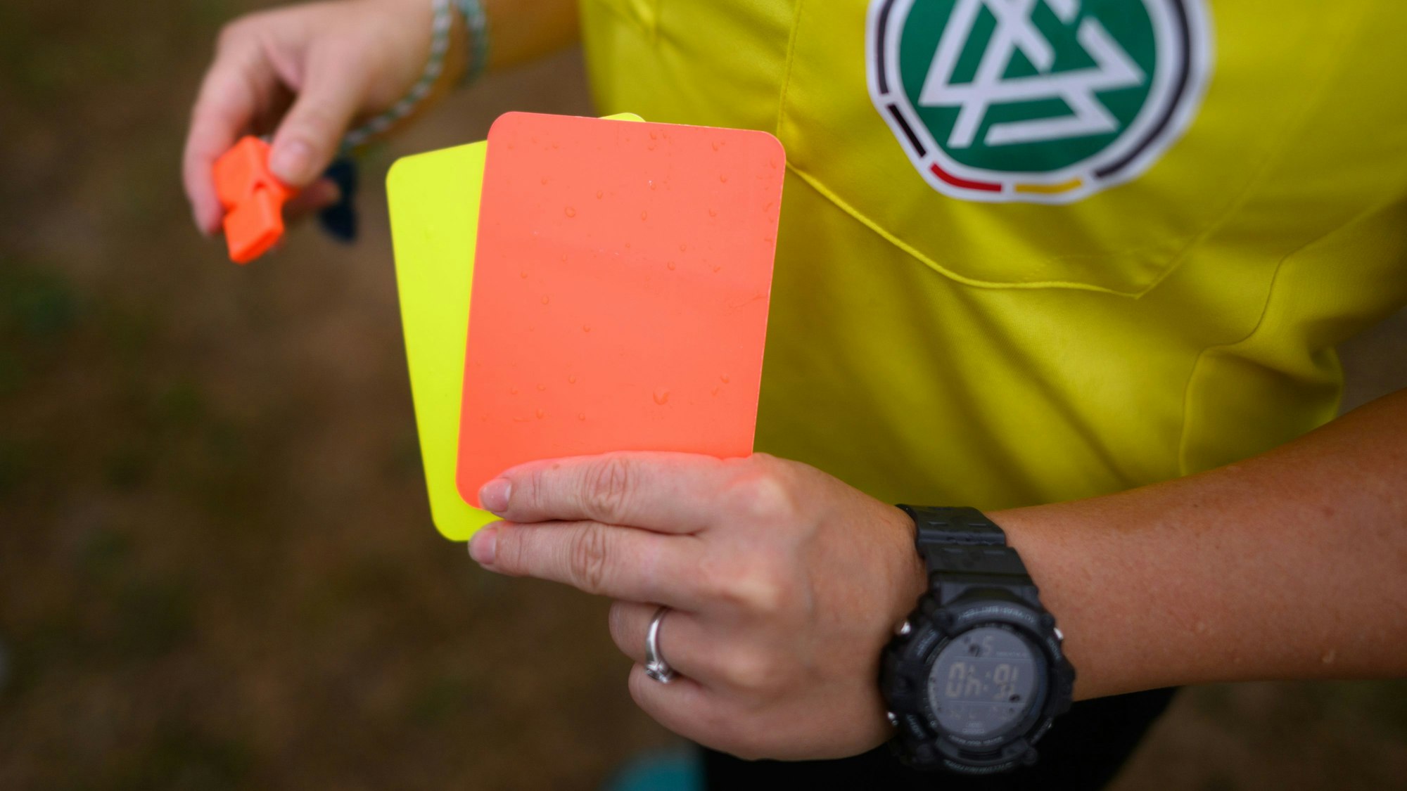 Eine Schiedsrichterin hält eine rote und gelbe Karte in der einen, und eine Trillerpfeife in der anderen Hand.