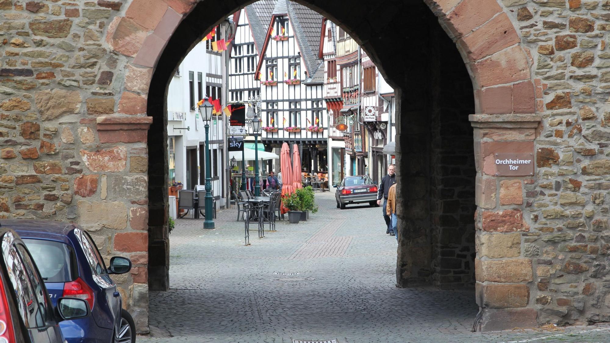 Die Innenstadt von Bad Münstereifel im Jahr 2013, durch das Orchheimer Tor fotografiert. Vor demTor parken Autos. Ein Wagen fährt im Hintergrund über die Orchheimer Straße.