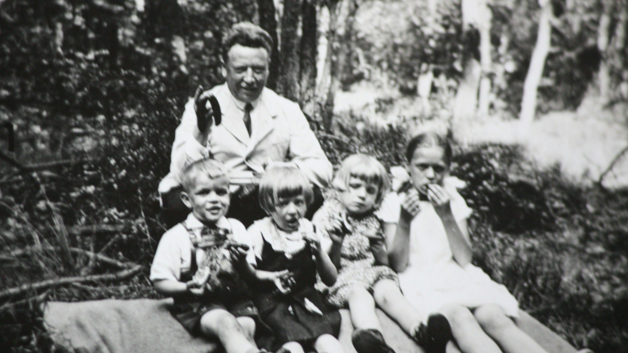 Edmund Schiefeling sitzt gemeinsam mit vier Kindern auf einer Decke beim Picknick im Wald.