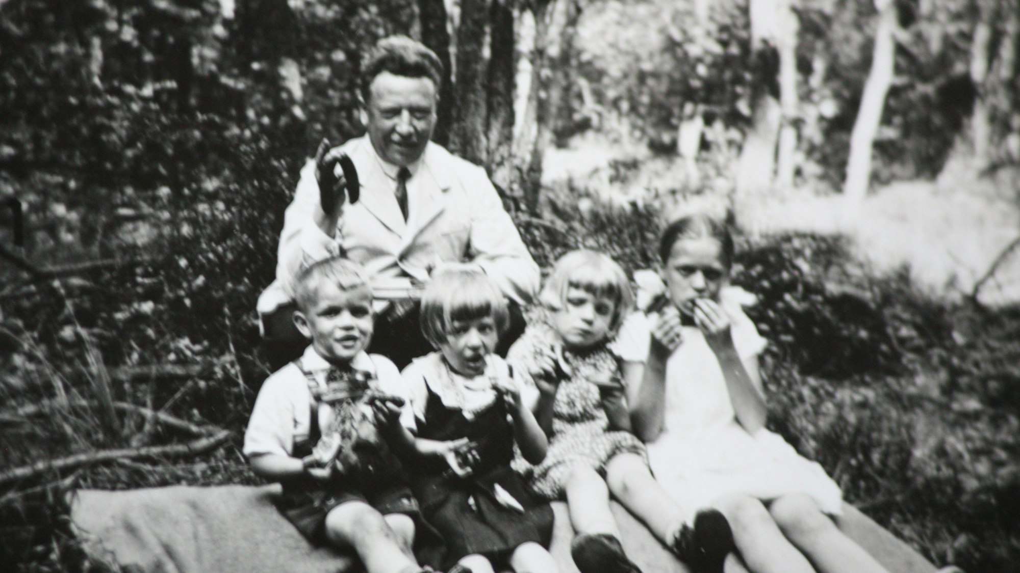 Edmund Schiefeling sitzt gemeinsam mit vier Kindern auf einer Decke beim Picknick im Wald.