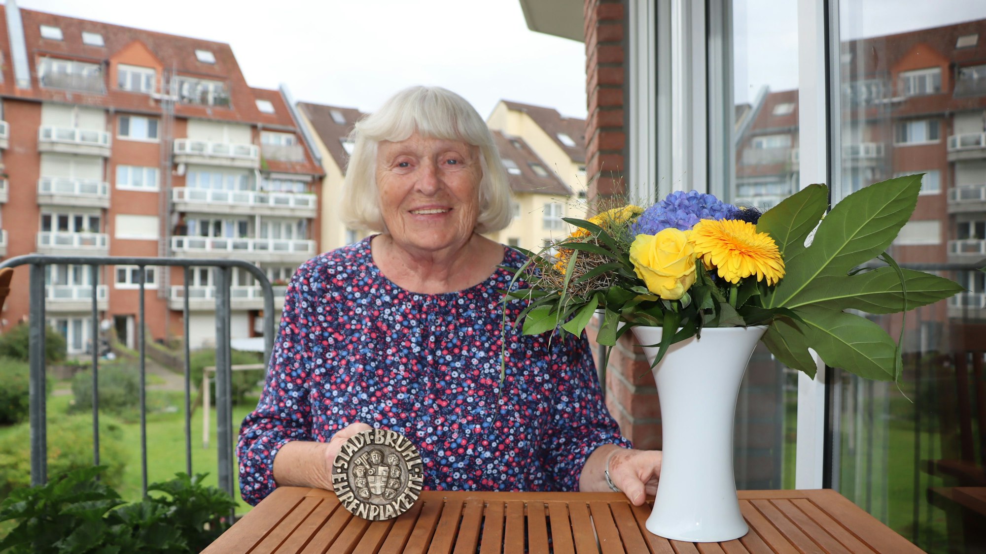Eine Frau hält eine Plakette ins Bild, darauf steht "Stadt Brühl - Ehrenplakette".