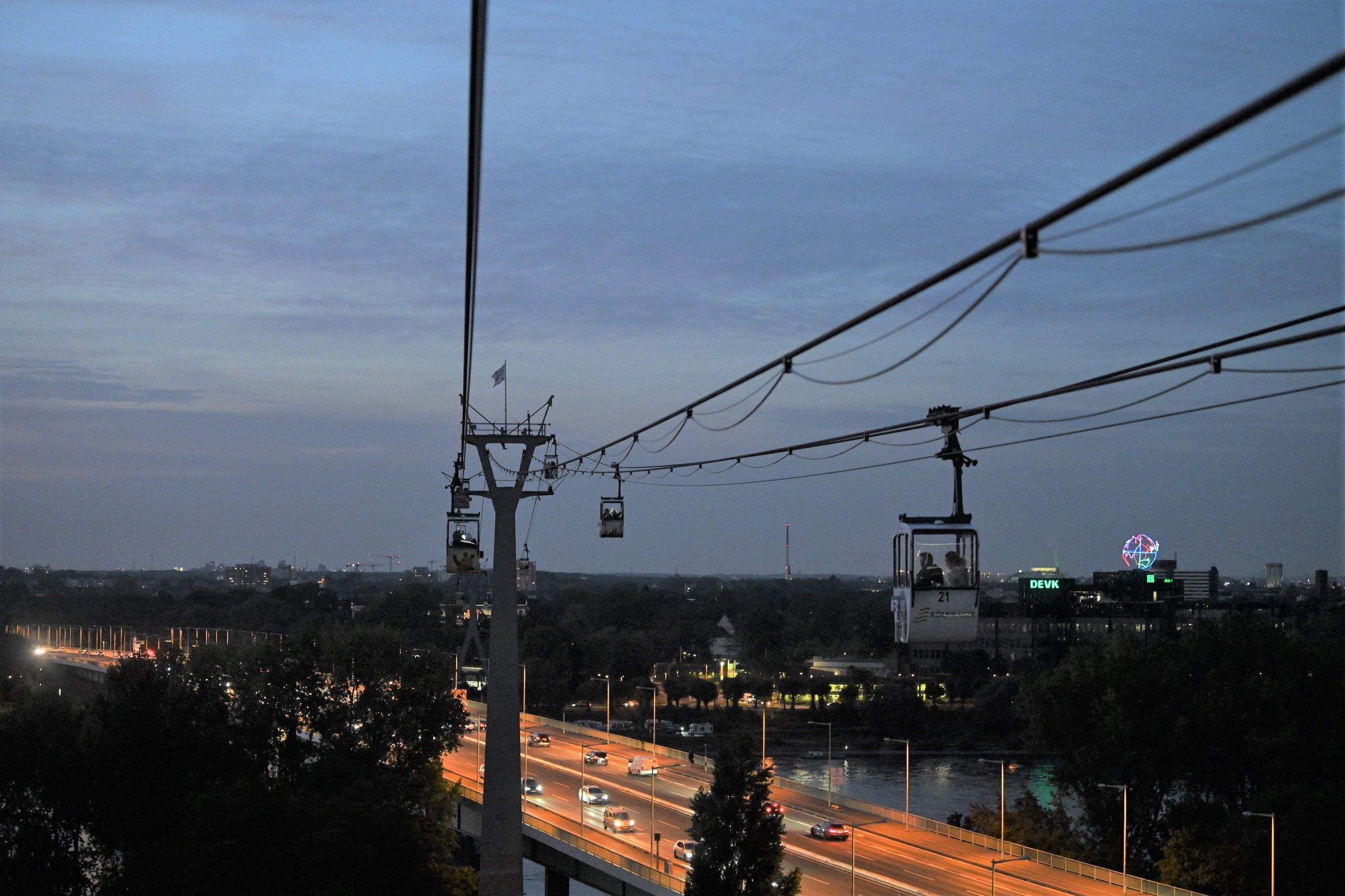 Blick aus einer Seilbahngondel in der Dämmerung auf die Zoobrücke und das linksrheinische Ufer.