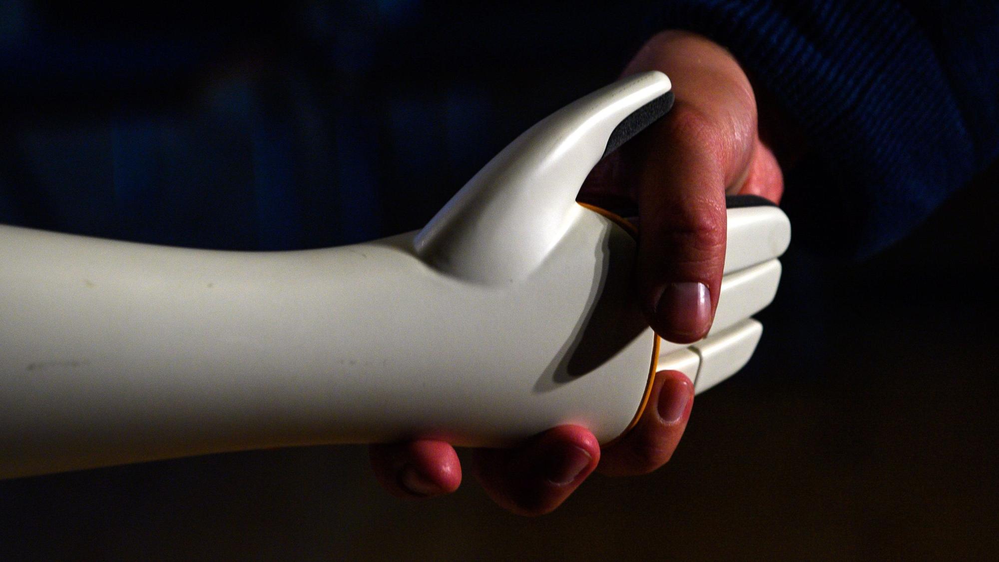 Eine menschliche Hand greift die Hand eines humanoiden Roboters.