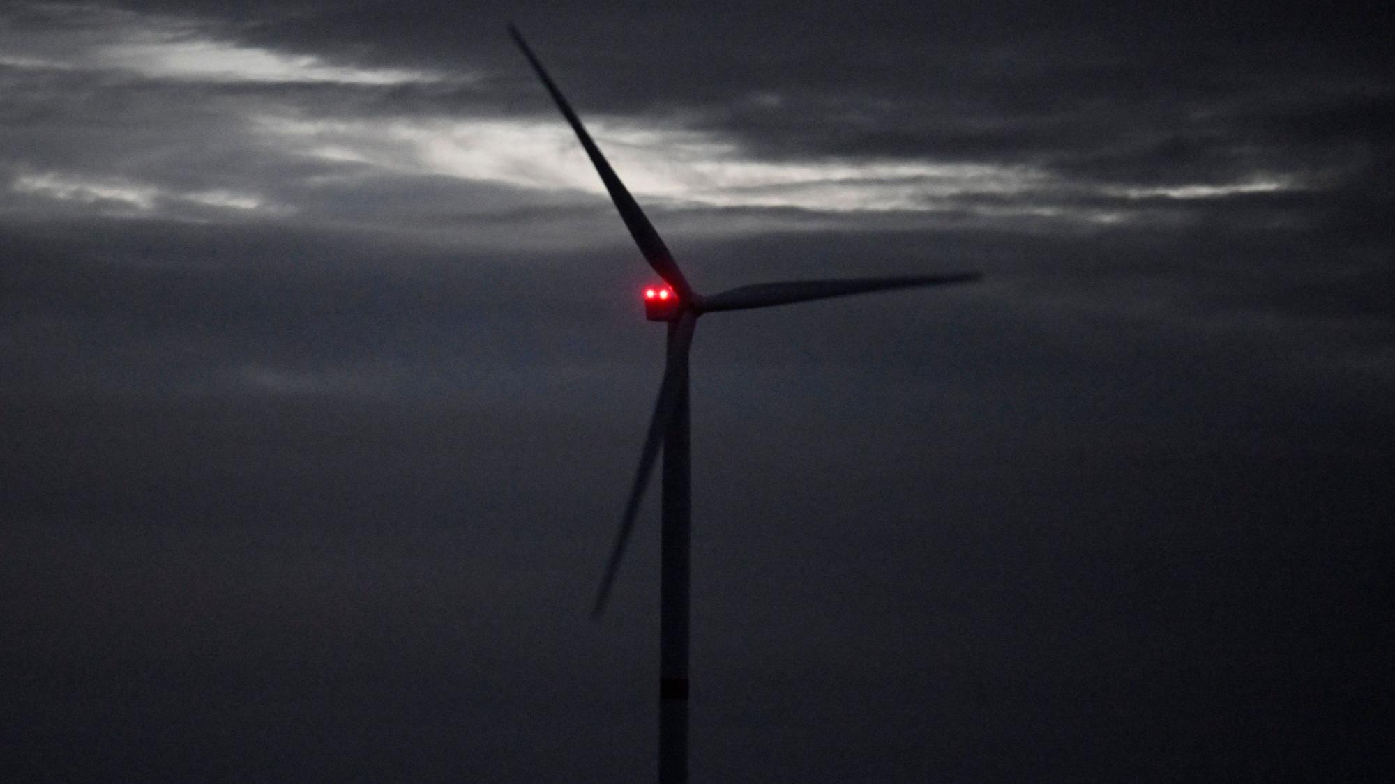 Ein Windrad dreht sich vor einem Unwetter im Wind. Hinter seinen Rotorblättern ist eine rote Leuchte zu sehen.