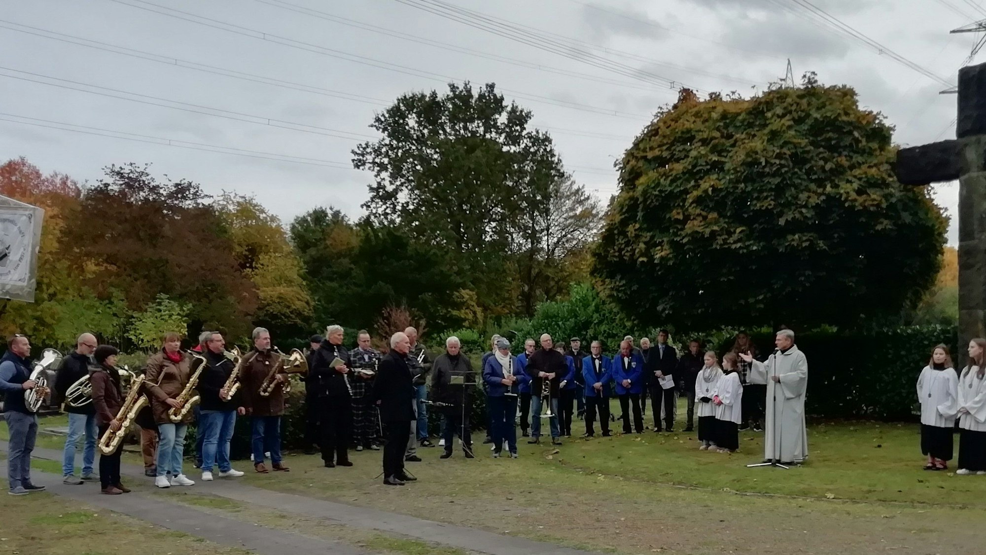 Eine Gruppe von Blasmusikern und Geistlichen auf dem Friedhof.