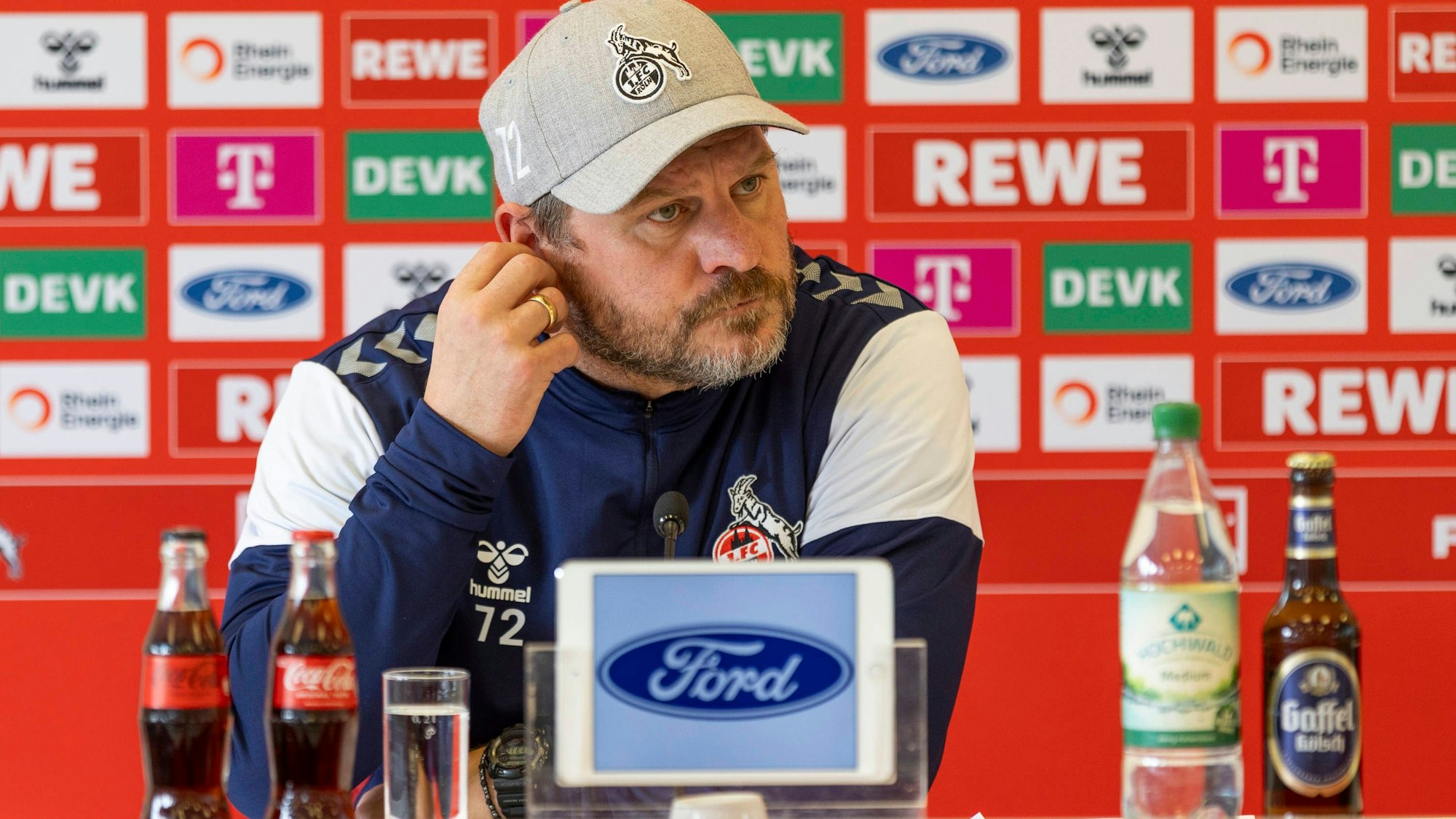 Steffen Baumgart sitzt vor einer großen Werbewand.