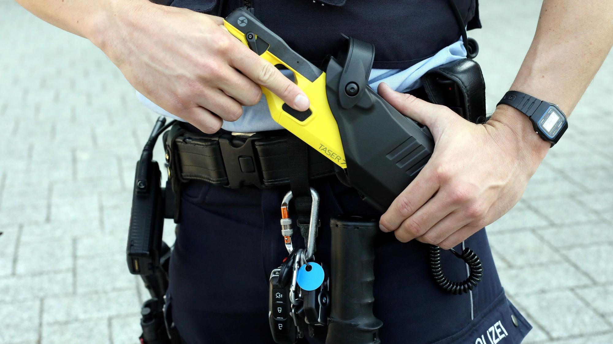 Ein Kölner Polizist zieht eine Elektroschock-Waffe aus dem Gürtel.