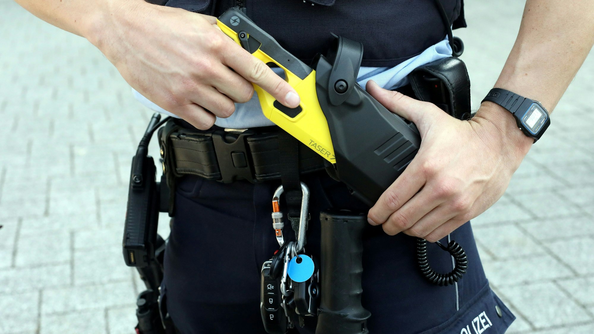 Ein Kölner Polizist zieht eine Elektroschock-Waffe aus dem Gürtel.
