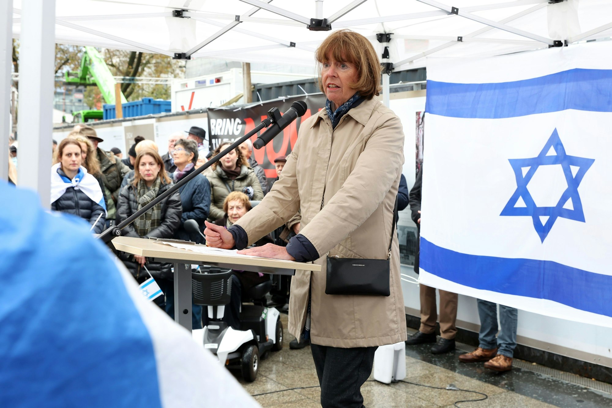 Oberbürgermeisterin Henriette Reker steht an einem Rednerpult, hinter ihr ist eine Israel-Flagge.