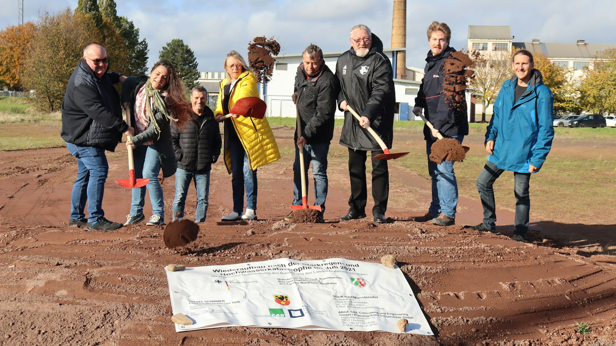 Vertreter aus Vereinen, Politik, Verwaltung und Planer schleudern mit einer Schaufel Erde in Richtung der Kamera.
