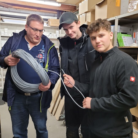 Zu sehen sind ein Erwachsener und zwei Jugendliche, die sich ein aufgerolltes meterlanges Kabel anschauen.