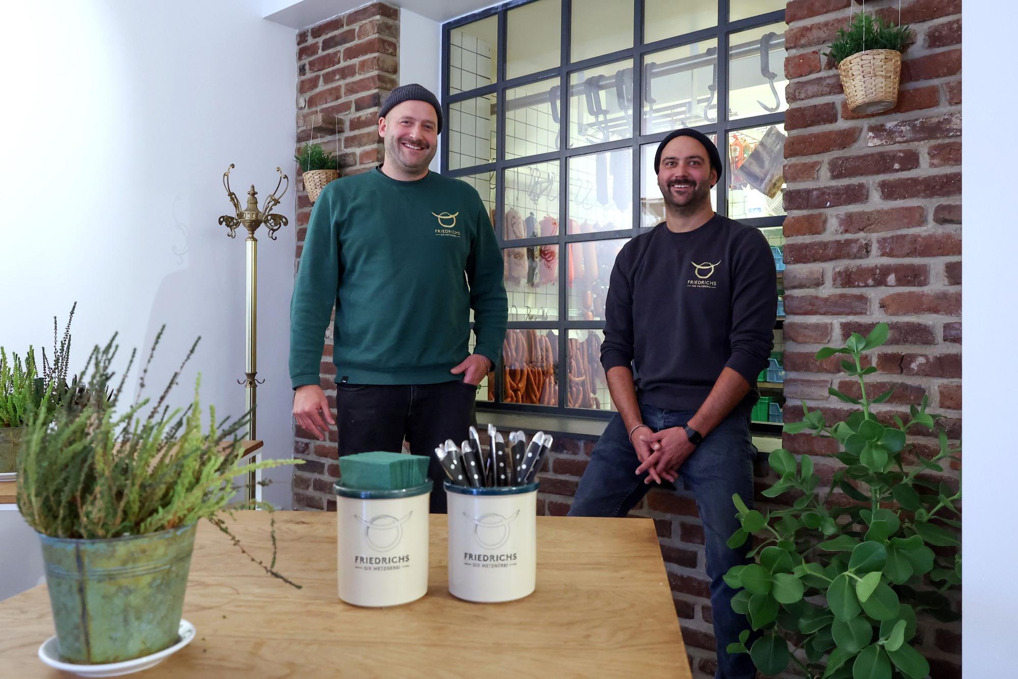 Die Brüder David und Sebastian Friedrichs sitzen vor einem gläsernen Kühlhaus.