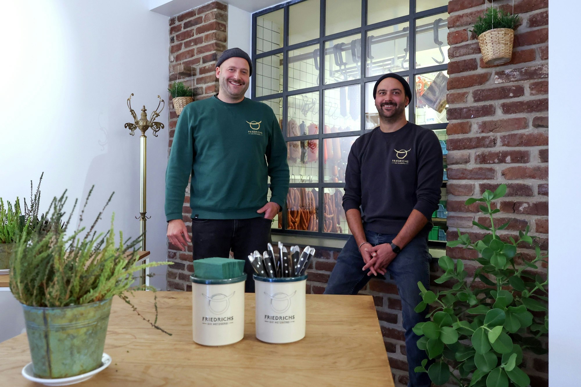 Die Brüder David und Sebastian Friedrichs sitzen vor einem gläsernen Kühlhaus.