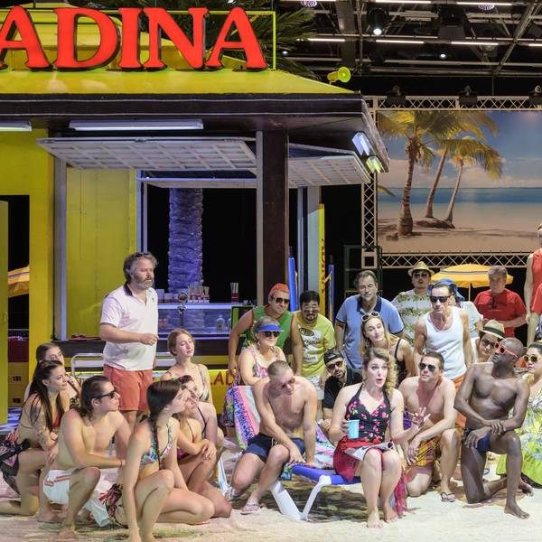 Auf der Bühne ist eine Strandszene zu sehen. Die zahlreichen Darstellerinnen und Darsteller tragen Badekleidung.