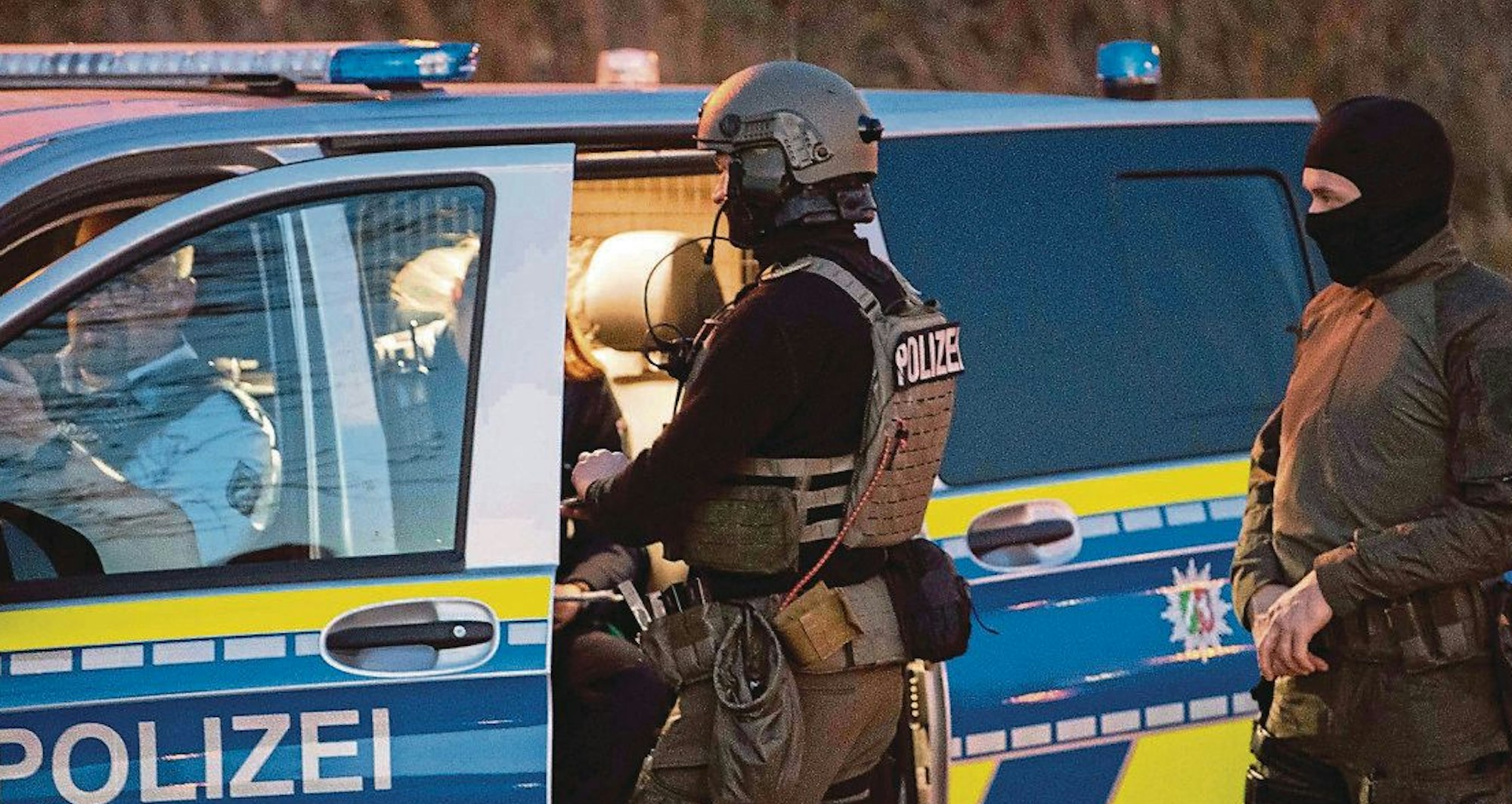 Auf dem Foto sind Mitglieder eines Spezialeinsatzkommandos zu sehen. Sie stehen an einem Polizeiwagen.