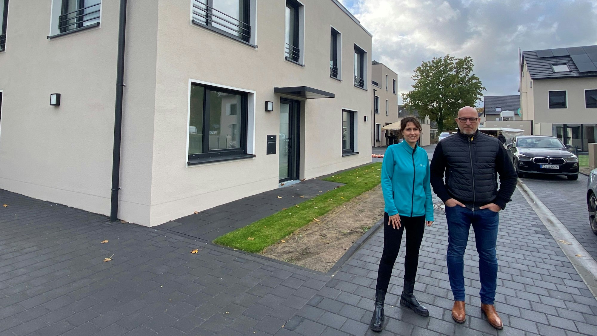 Eine Frau und ein Mann stehen in einer Neubausiedlung auf dem gepflasterten Fußweg.