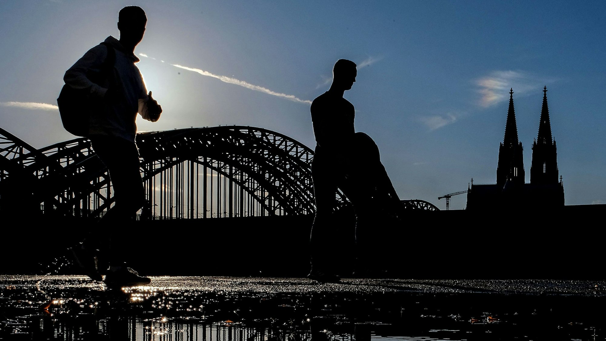 24.10.2023, Nordrhein-Westfalen, Köln: Zwei Männer gehen nach einem regnerischen Tag in der Abendsonne am Rheinufer entlang. Foto: Oliver Berg/dpa +++ dpa-Bildfunk +++
