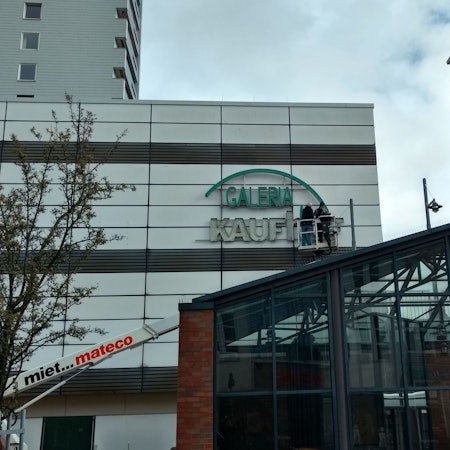 Arbeiter entfernen den Kaufhof-Schriftzug von der Fassade am Wiesdorfer Platz.
