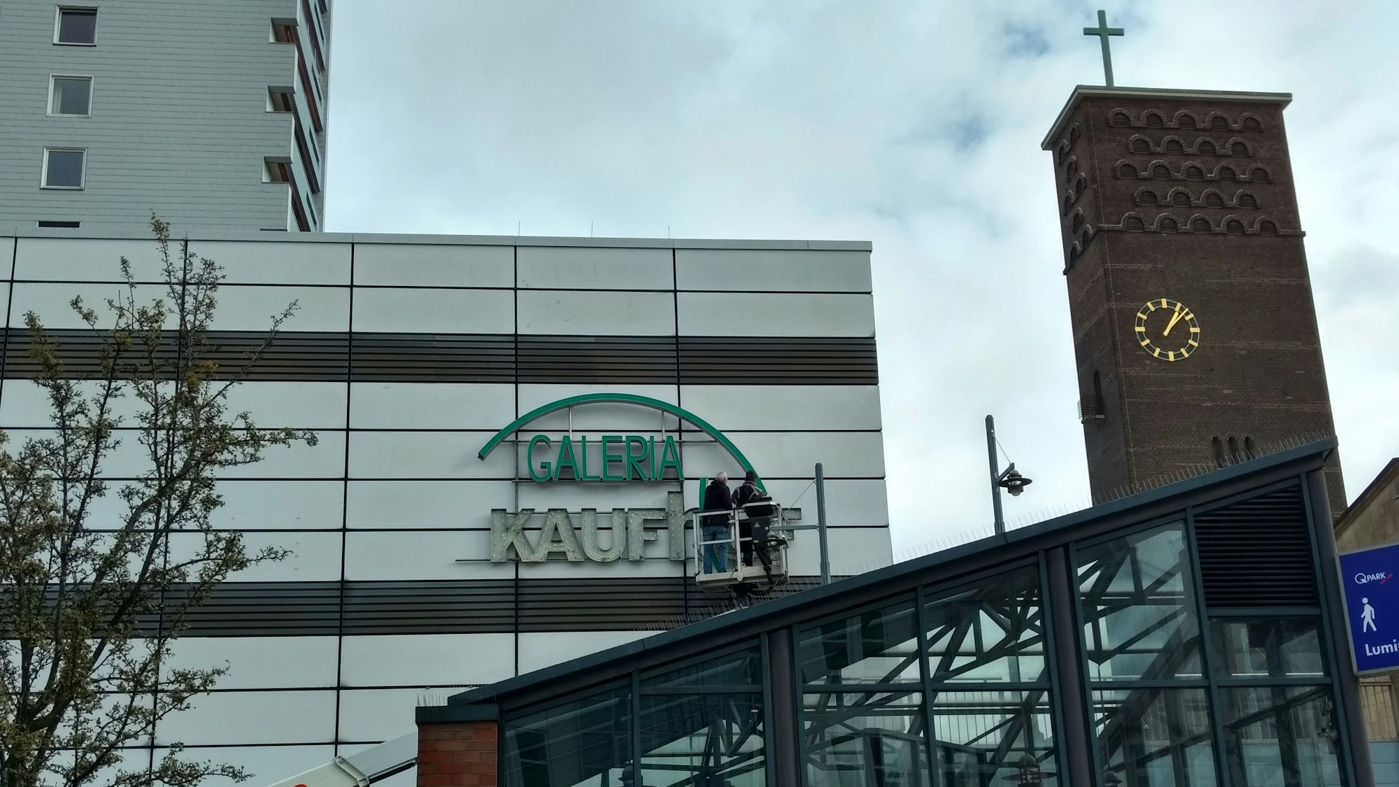 Arbeiter entfernen den Kaufhof-Schriftzug von der Fassade am Wiesdorfer Platz.