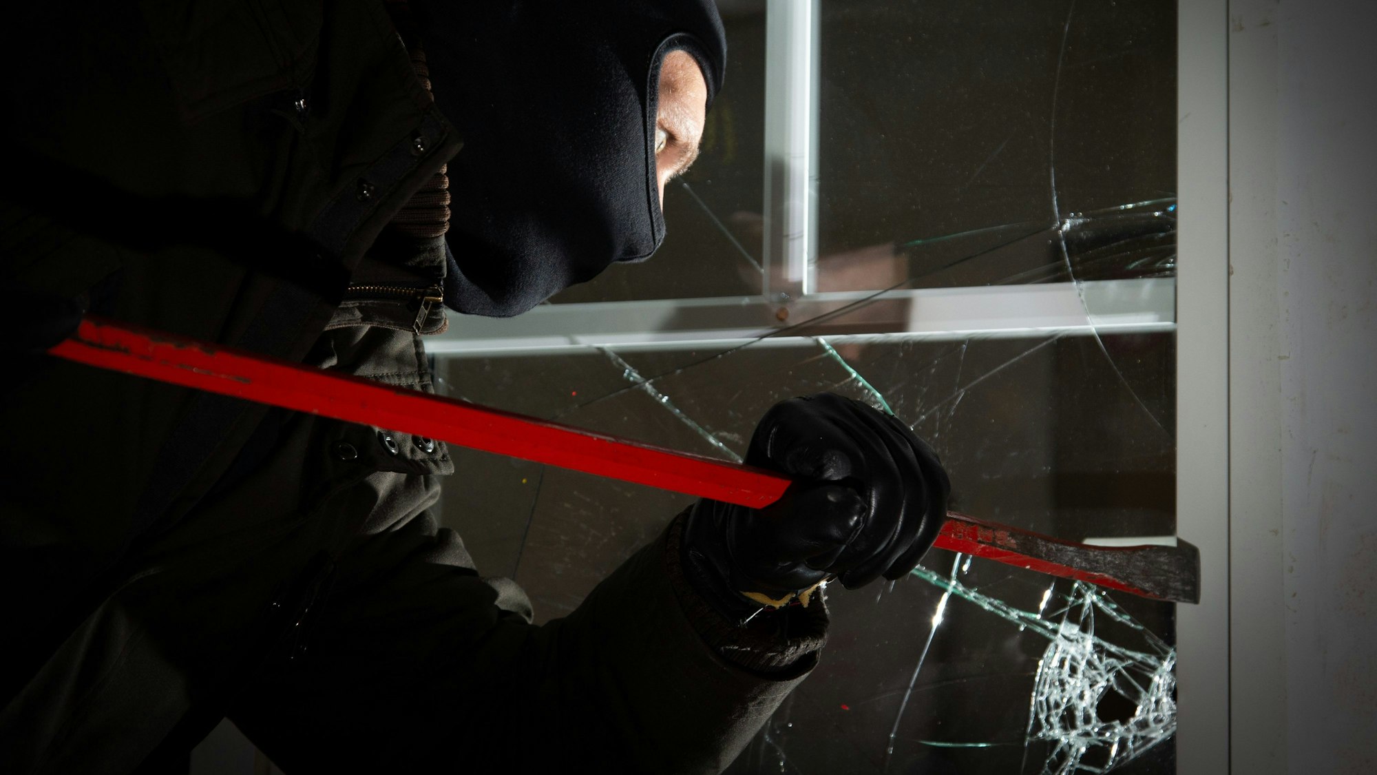 Ein als Einbrecher verkleideter Mann bricht mit einem Kuhfuß ein Fenster auf. In der dunklen Jahreszeit sind auch wieder mehr Einbrecher und Diebe unterwegs.