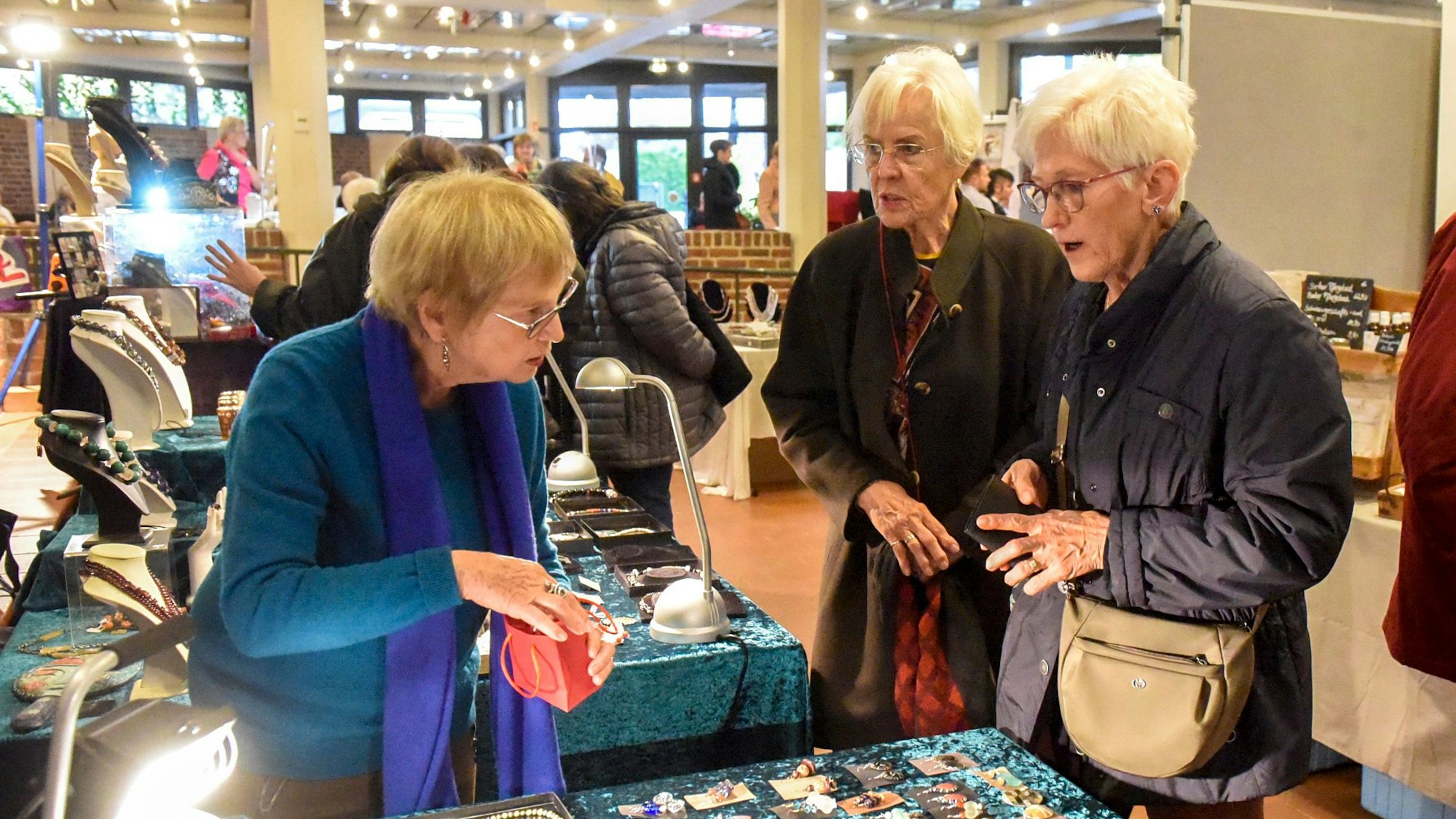 Besucherinnen des Handwerkermarktes sehen sich Schmuck an einem Stand an.