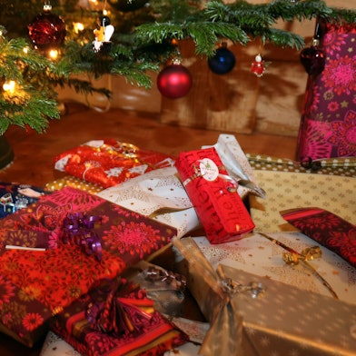 Verpackte Weihnachtsgeschenke liegen unter einem Christbaum.