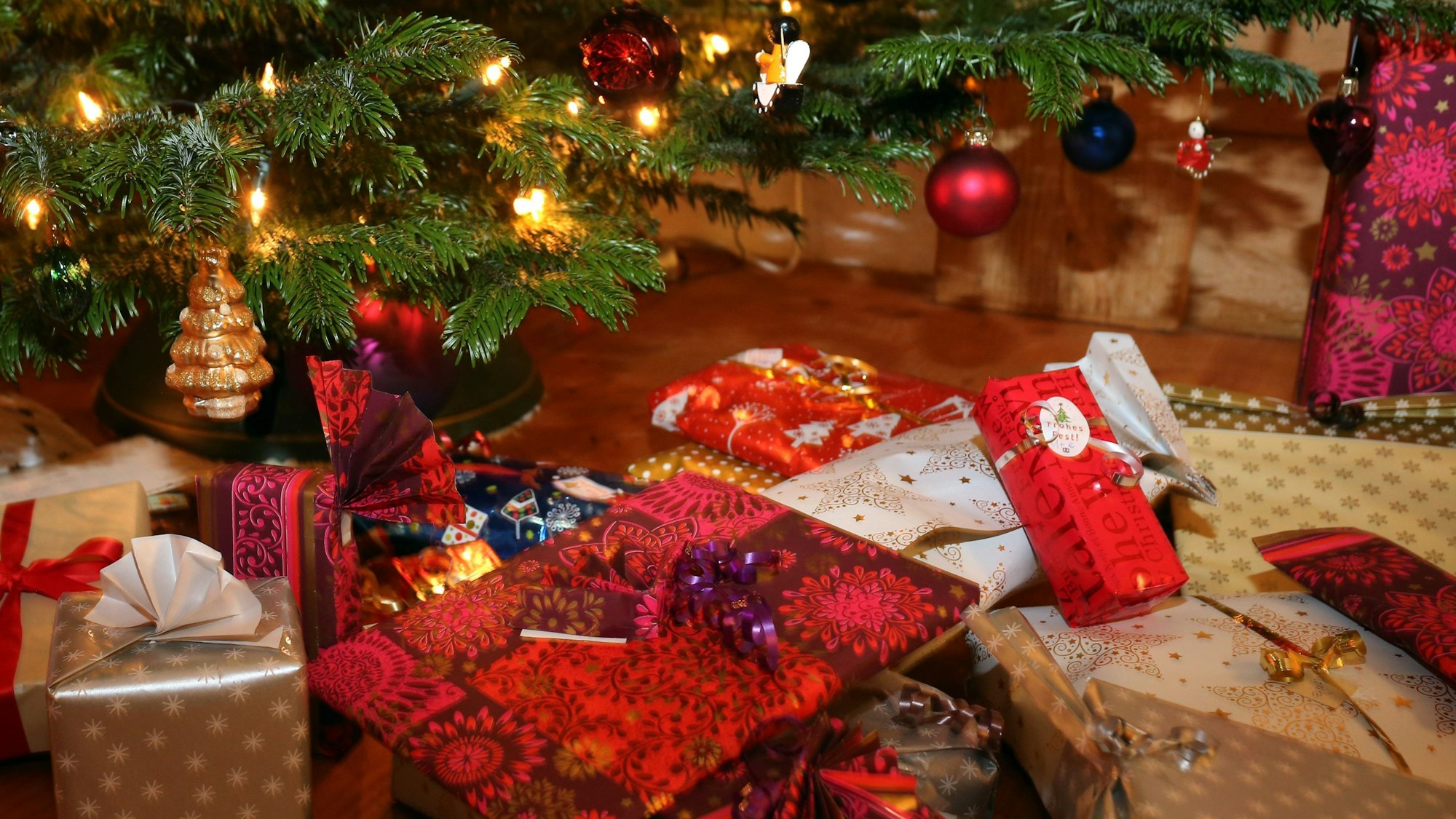 Verpackte Weihnachtsgeschenke liegen unter einem Christbaum.