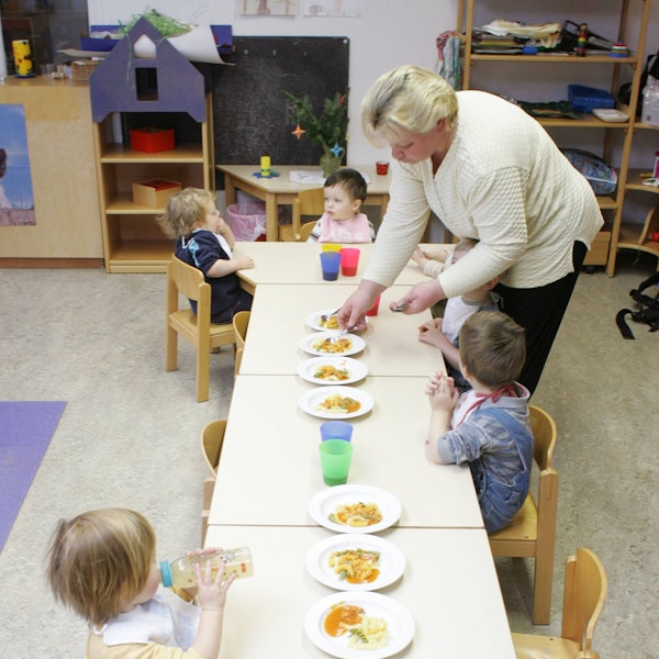Kinder mit Erzieherin beim Mittagessen