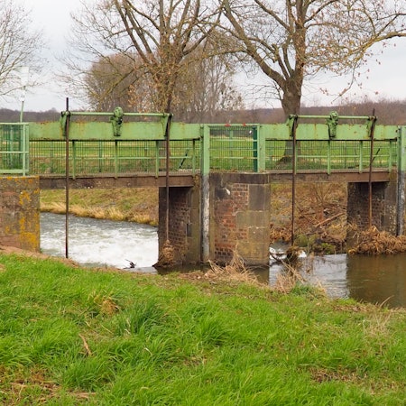 Ein Fluss mit schnurgeraden Ufern fließt durch ein Wehr.