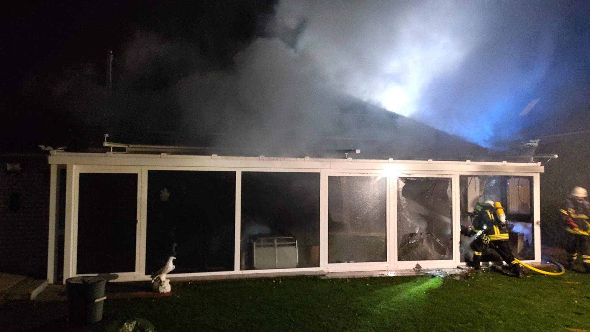 Zwei Feuerwehrleute rücken unter Atemschutz in einen Wintergarten vor, aus dem Rauch aufsteigt.