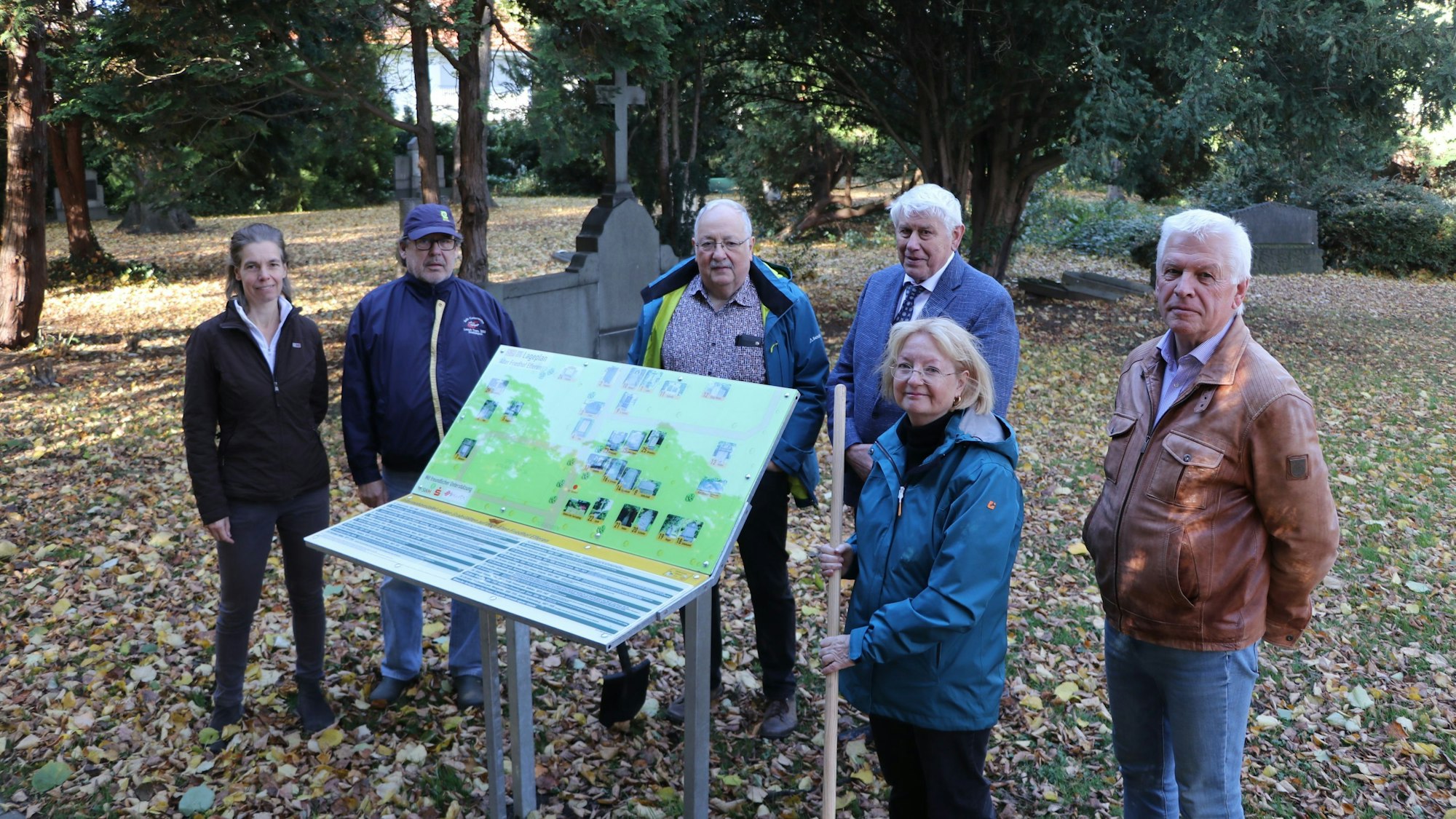 Eine Gruppe von Männern und Frauen hinter einer Infotafel auf dem Friedhof.