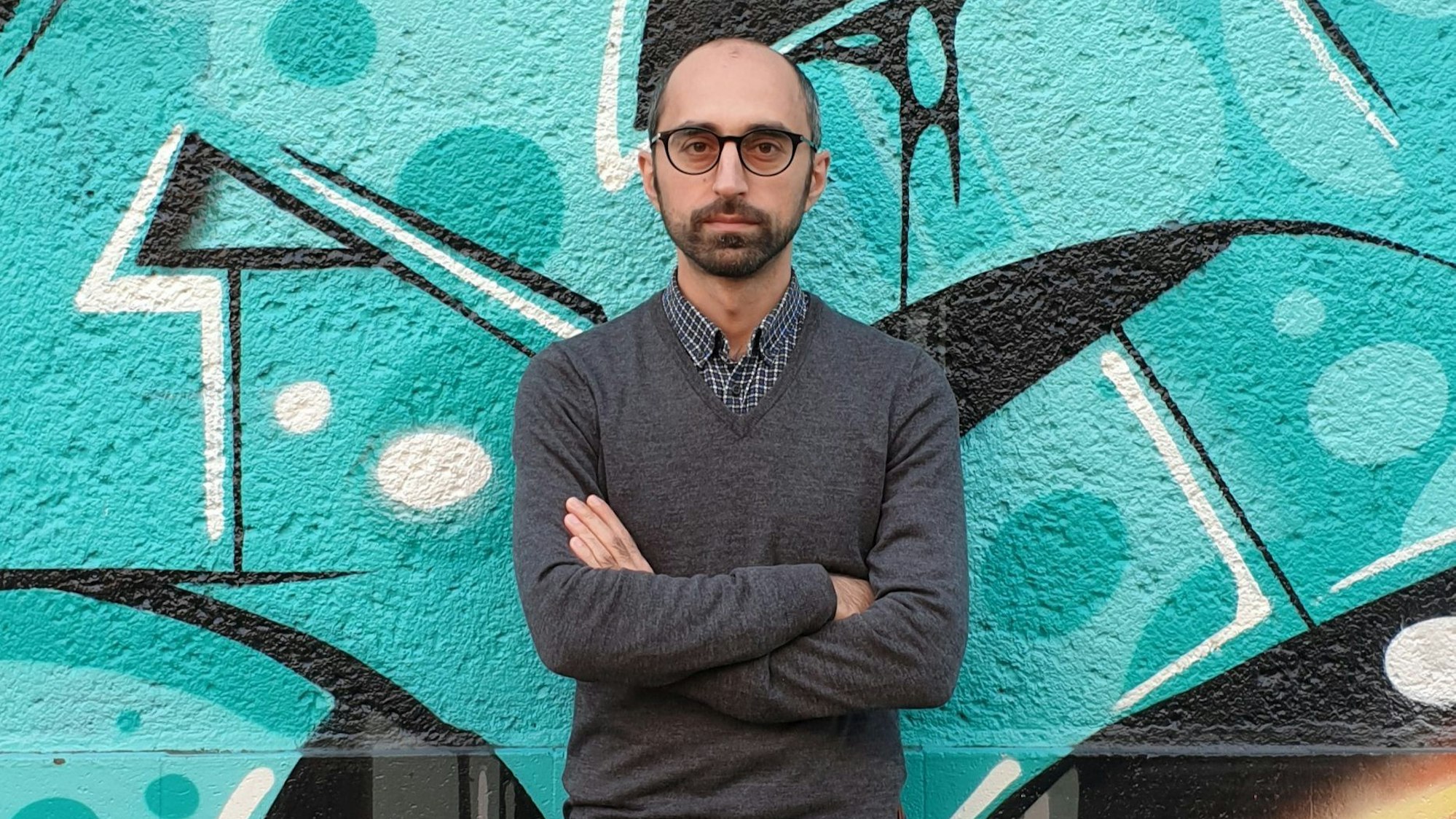Islamexperte Eren Güvercin mit verschränkten Armen vor einem Graffiti