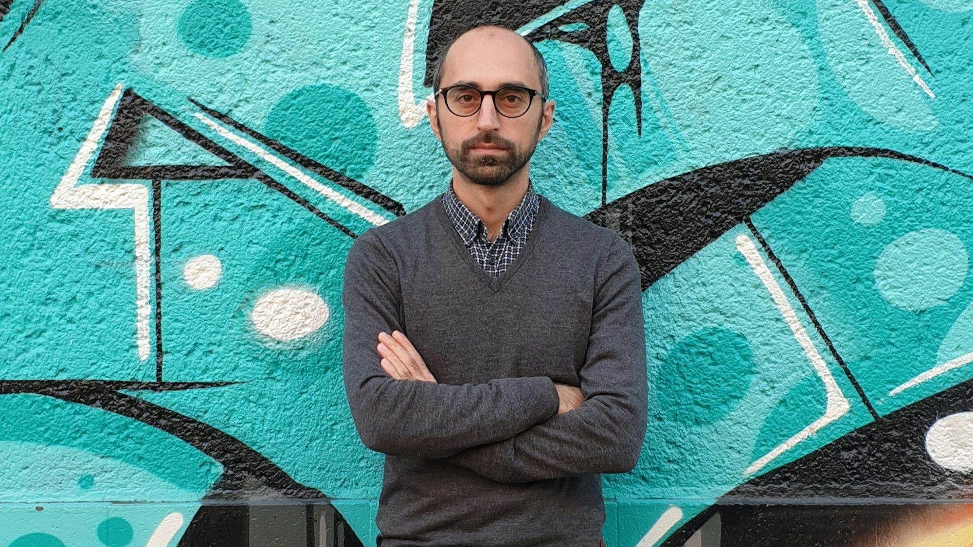 Islamexperte Eren Güvercin mit verschränkten Armen vor einem Graffiti