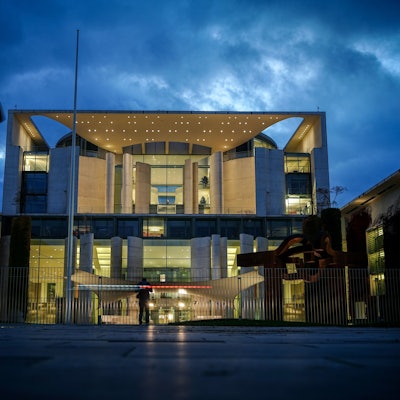 Das Bundeskanzleramt wird am Abend angestrahlt, vor ihm wehen eine Deutschland- und eine Europaflagge.